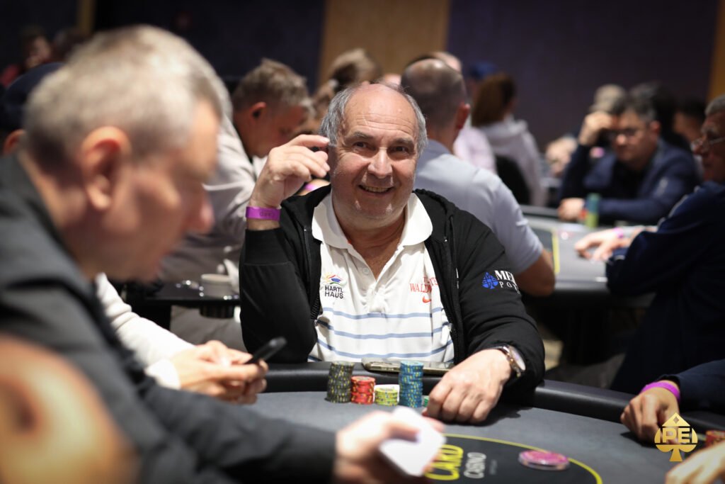 Ein Mann sitzt an einem Pokertisch, umgeben von Spielkarten und Chips. Er hält zwei Karten in der Hand und schaut konzentriert auf den Tisch.